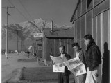 Roy Takeno, editor, and group reading paper in front of office, Manzanar Relocation Center, California