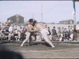 Two men grapple in the sumo ring in front of spectators.
