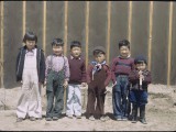 A group of children line up for a photo in front of a barrack wall. Billy Manbo is on the far right.