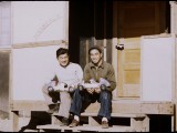 Bill Manbo (left) and a friend sit on Manbo’s front steps, showing off their model racing cars. Manbo used scrap lumber and Celotex wallboard to build a small sheltered porch on the landing in front of his barrack door. On the outer wall to the left of the door, he wrote his family name, spelling it "Manbeaux" as if it were French.